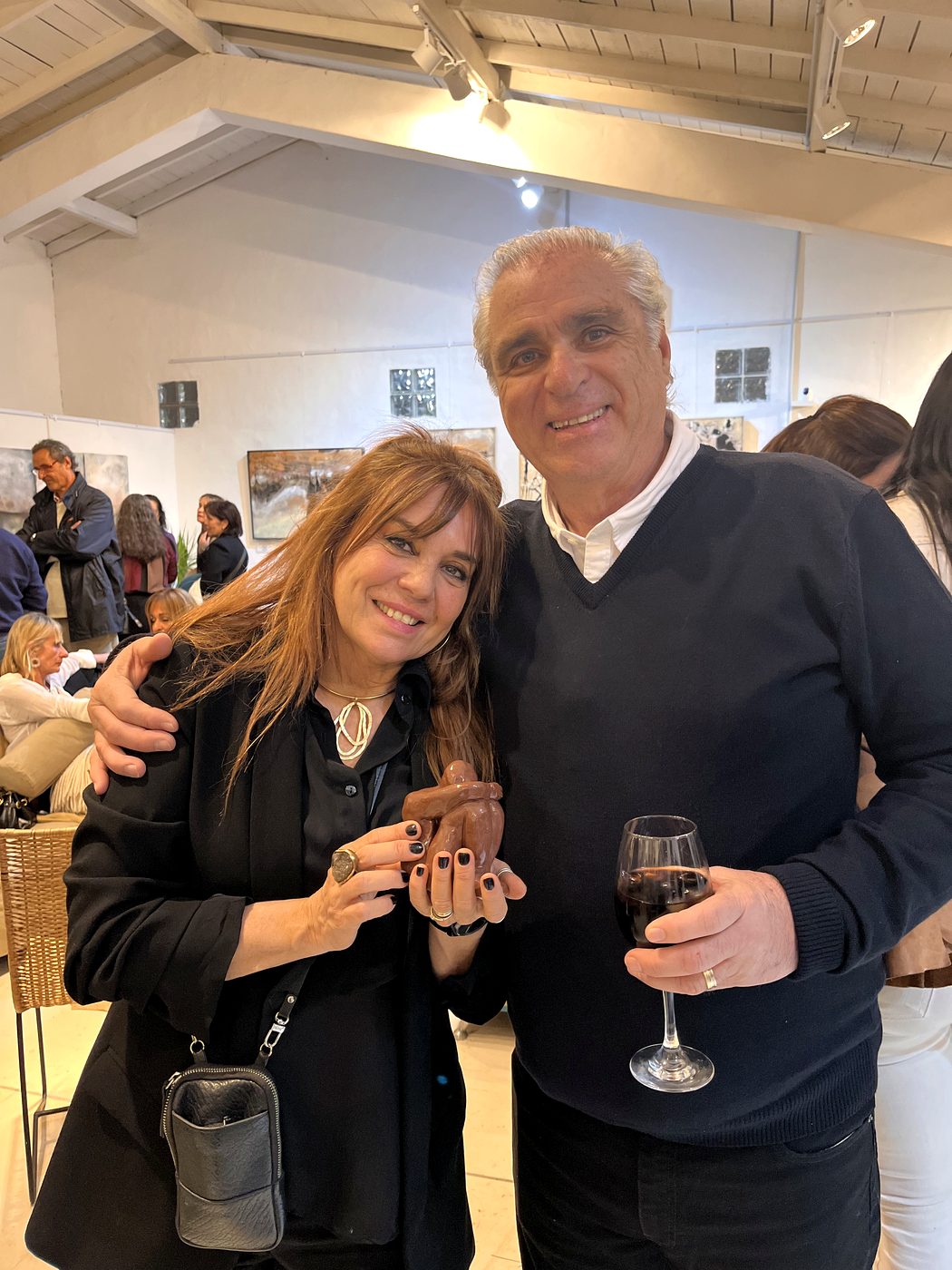Vale Marini y su marido César abrazados en la sala de la muestra, ella sostiene un Tipito de cerámica