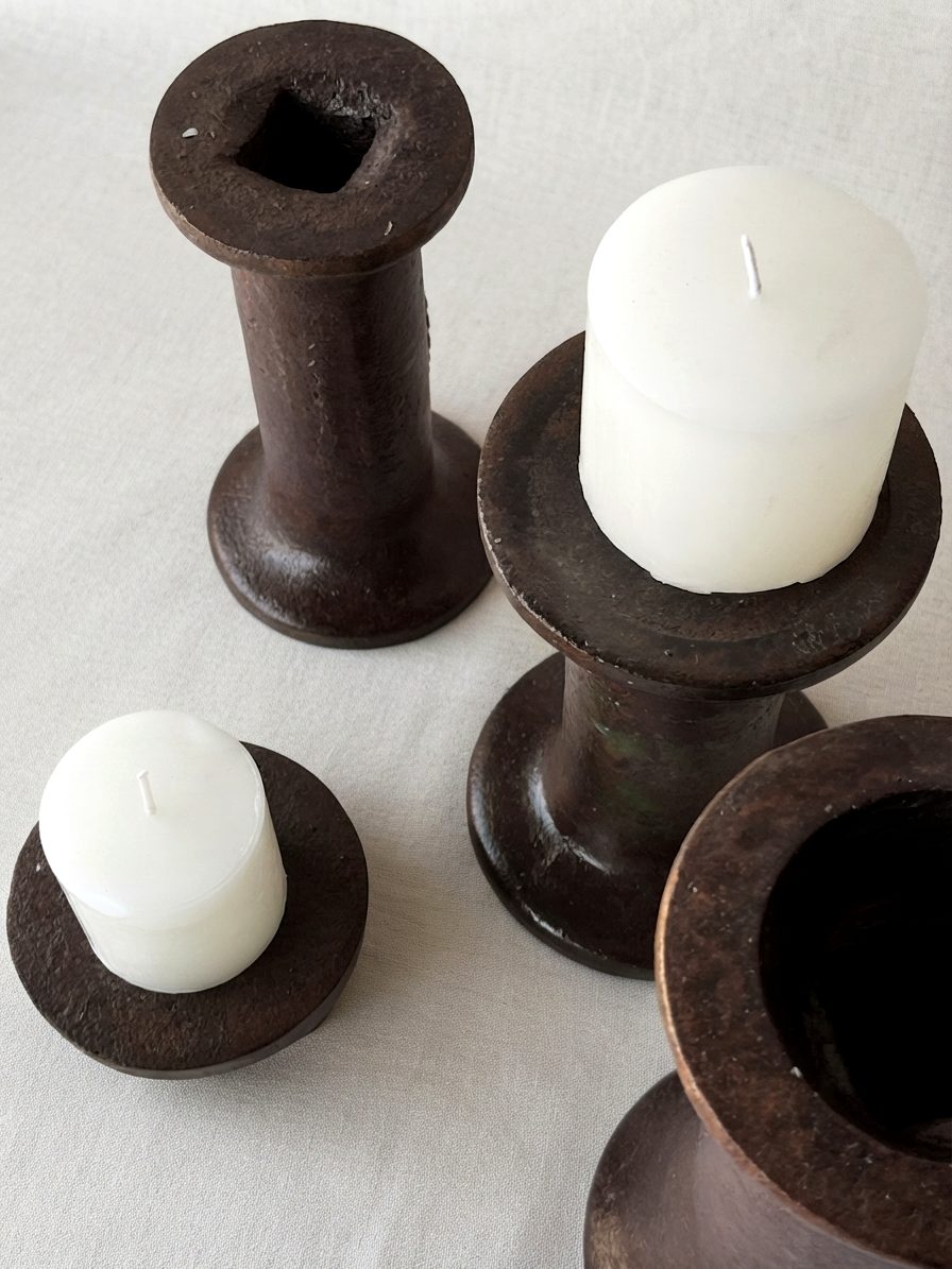 Cuatro carreteles de hierro oxidado usados como candeleros con velas blancas