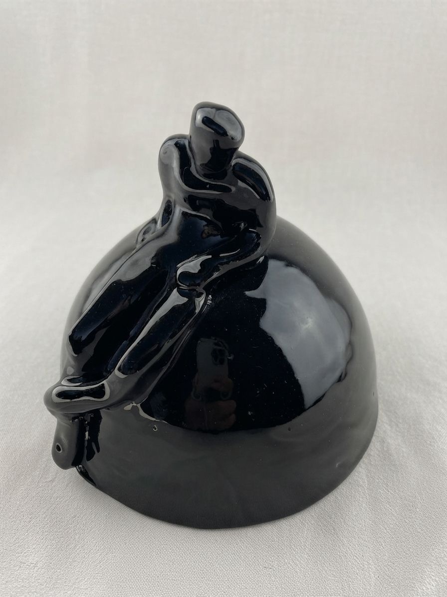 Dos figuras de cerámica negra brillante sentadas juntas al borde de una colina redondeada