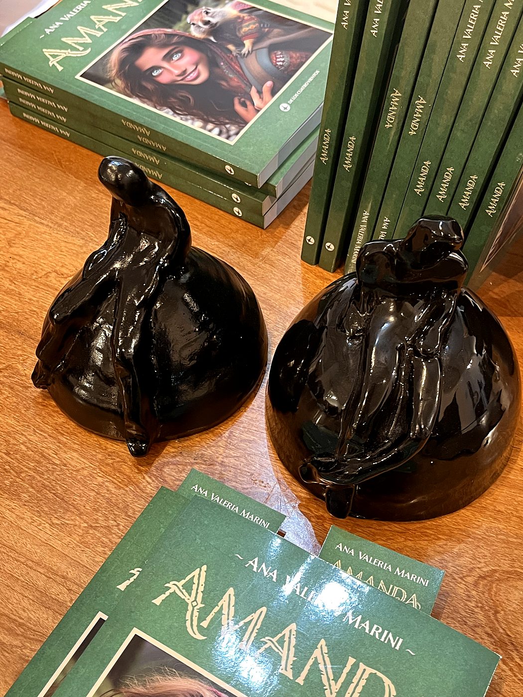 Dos Tipitos de cerámica negra brillante sobre una mesa de madera rodeados de ejemplares del libro Amanda