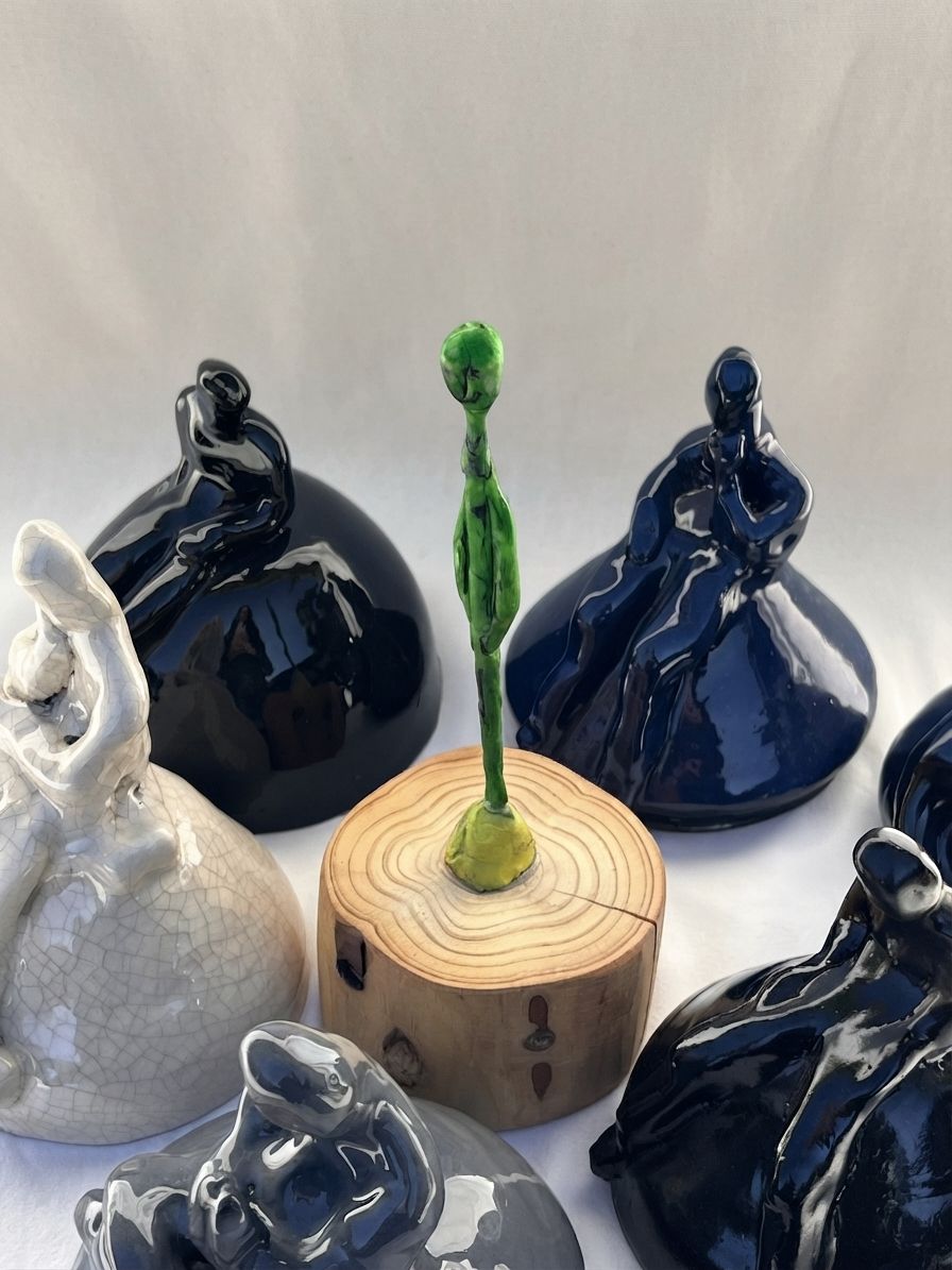 Conjunto de varias figuras de cerámica de distintos colores junto a un brote verde sobre un tronco de madera
