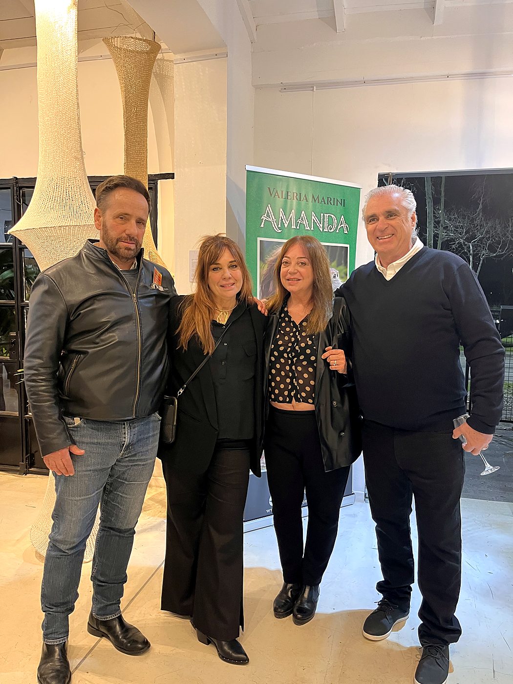 Cuatro personas posan junto al banner del libro Amanda en la entrada de la muestra