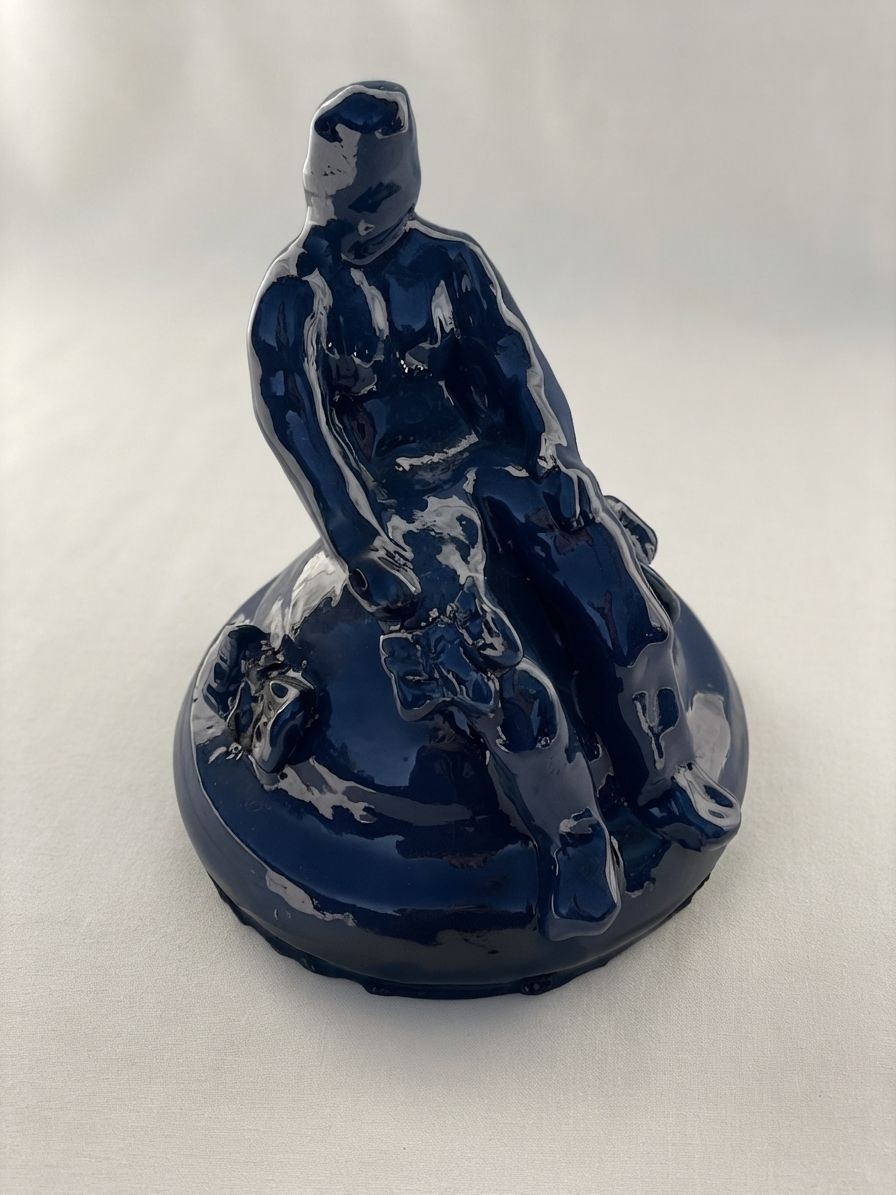 Figura de cerámica azul marino brillante sentada en la cima de una base redondeada, con los hombros relajados