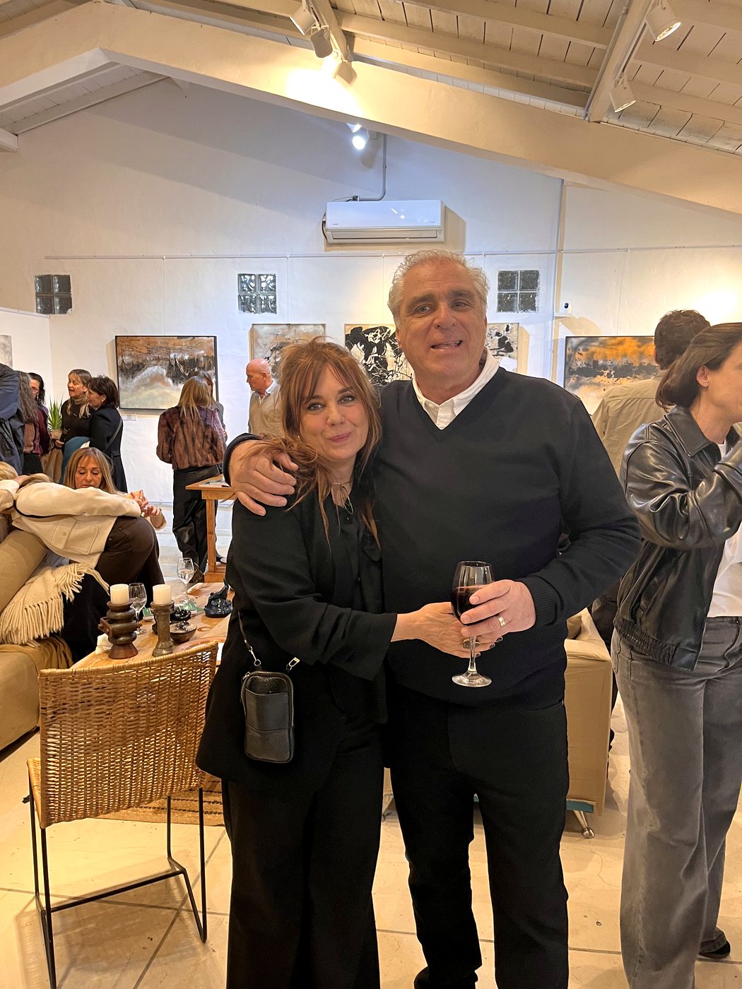 Vale Marini y César abrazados en el centro de la sala, con las obras y los visitantes alrededor