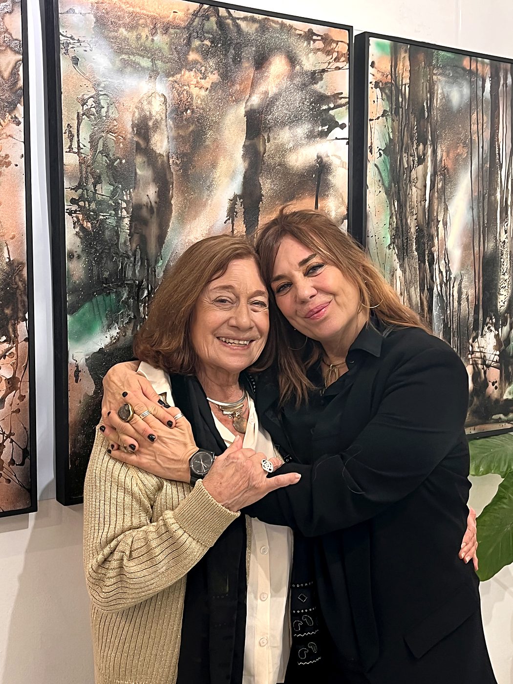 Vale Marini abrazada a una visitante delante de dos grandes pinturas de la serie Llamados de la Tierra