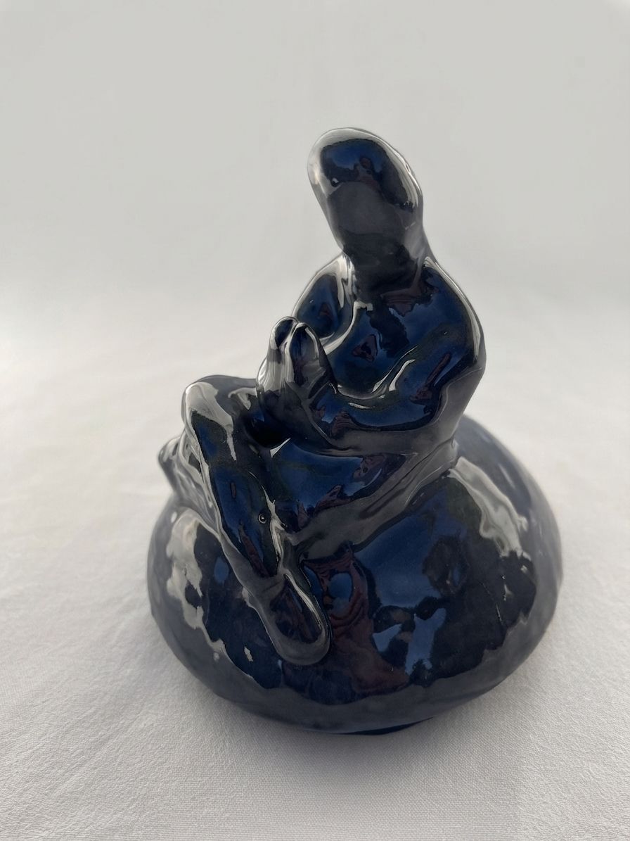 Figura de cerámica azul con vetas granate, sentada con las manos sobre las rodillas