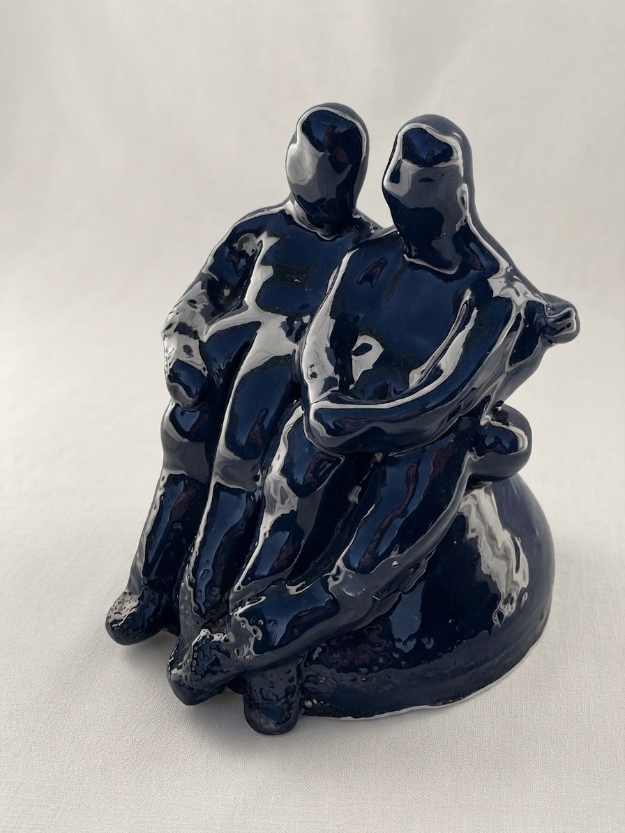 Dos figuras de cerámica azul marino sentadas juntas, con las cabezas apoyadas una junto a la otra