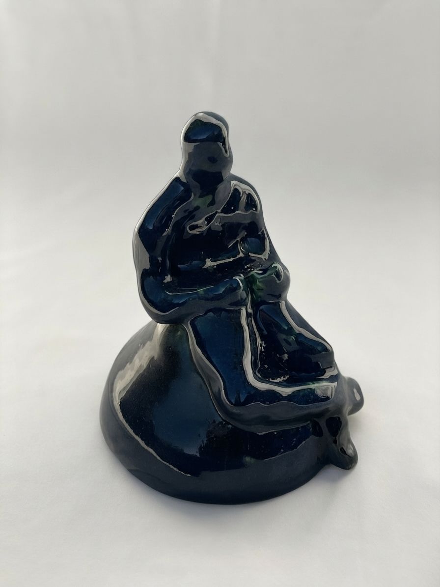 Figura de cerámica azul muy oscura con reflejos verdes, envuelta en un pliegue como manto