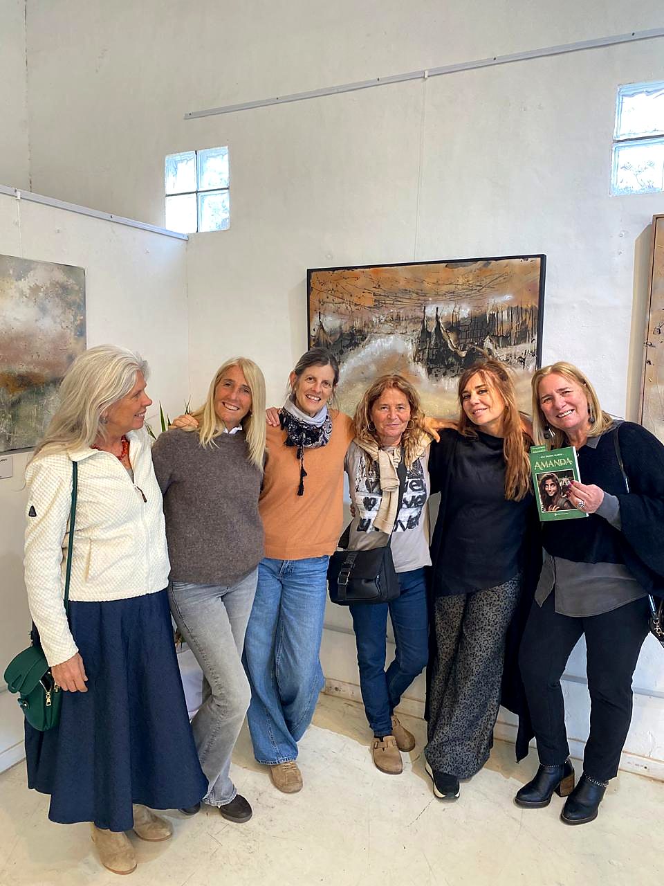 Seis mujeres posan sonrientes en la sala de la muestra, una de ellas con el libro Amanda en la mano