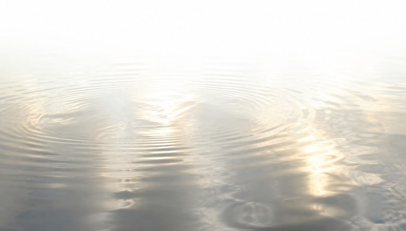 Superficie de agua en calma reflejando un cielo blanco, con ondas suaves